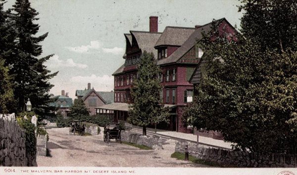 postcard of a four story red building, tall trees and stone fence along sidewalk