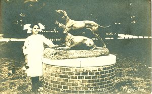 young girl next to statue of 2 hunting dogs. statue is on a pedestal, making it taller than the girl