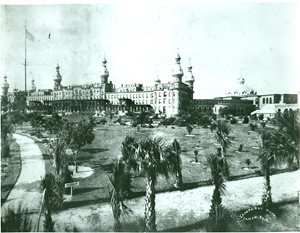 historic photo of Tampa Bay Hotel with gardens in foreground. American flag on flagpole in gardens