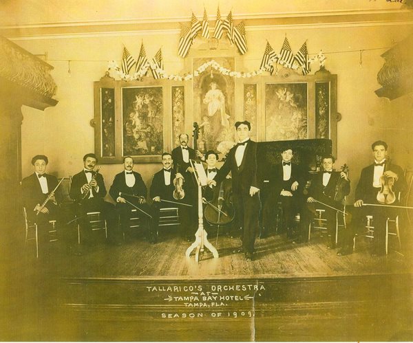 historic photo of men seated on stage holding string instruments, one man standing in foreground