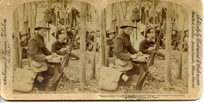 historic stereoscope card showing soldier, seated in forest, writing a letter, his gun propped up on a tree.