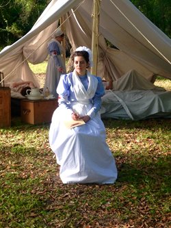 Young woman in historic nursing attire seated in front of 1890s style tent.