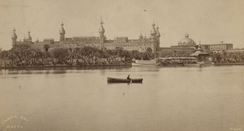 historic photo of Hotel from across river, man in rowboat in river, boathouse visible on right side of Hotel near the water