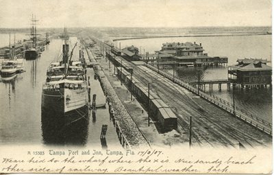historic postcard, train tracks extending on a pier into a bay, large ships on left of tracks, building on piers over water on right of tracks