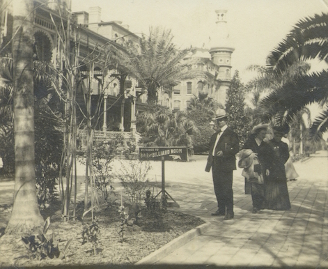 1 man and 2 women standing in front of hotel next to small sign reading "Bar & Billiards Room"