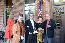 group of 2 men and 2 women standing on veranda, one couple in vintage 1890s clothing, the other in business attire
