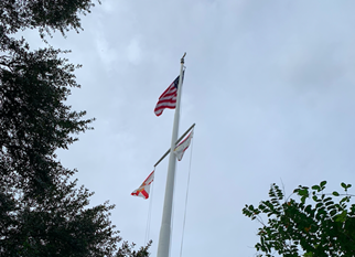 modern photo of flagpole. American flag at top, Florida State flag and unidentifiable flag underneath.
