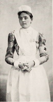 young woman standing with hands clasped wearing nurses uniform, red cross symbol on armband