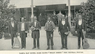 6 African American men in suits standing in a line holding instruments in front of the Tampa Bay Hotel veranda