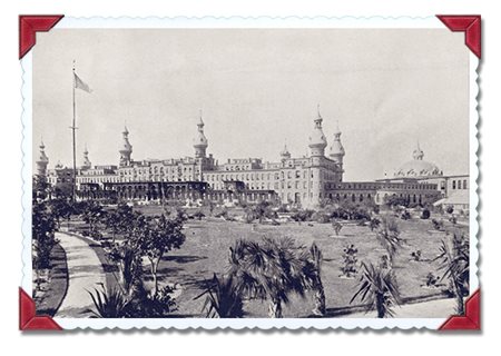 Tampa Bay Hotel seen from a distance, grounds with many plants and a flagpole in foreground