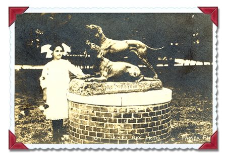 small girl in a white dress standing next to a large bronze statue of two dogs