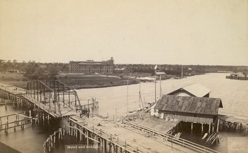 historic photo showing swing bridge over river. Hotel under construction in background