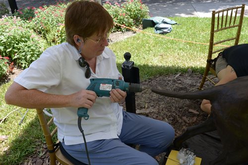 Woman using electric drill to attach a piece of tail of dog sculpture.