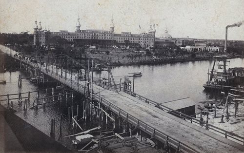 historic photo of bridge over Hillsborough River. Hotel in background, large smokestack on far right near river.